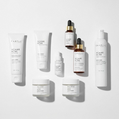 A variety of skincare products for acne treatment laid out on a minimalist white background, including tubes, bottles, and jars